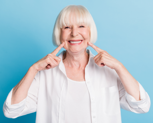 Senior woman smiling and pointing to her healthy teeth.
